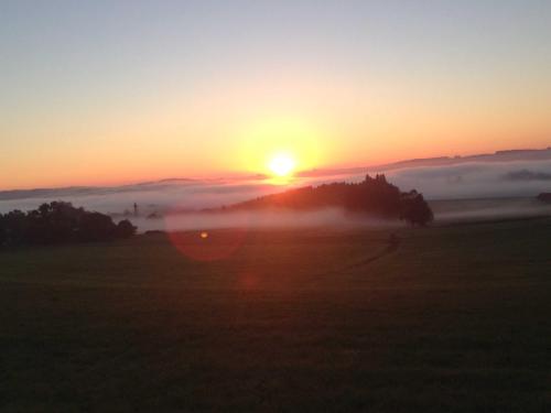 una puesta de sol con el sol saliendo sobre un campo en Ferienwohnung Ernle, en Bad Wurzach