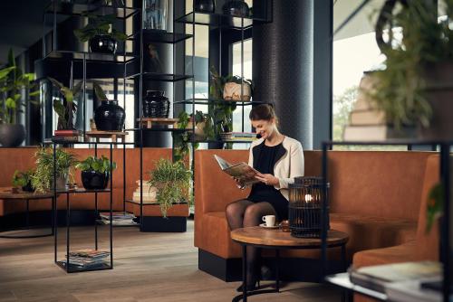 a woman sitting on a bench reading a book at Van Der Valk Luxembourg Arlon in Arlon