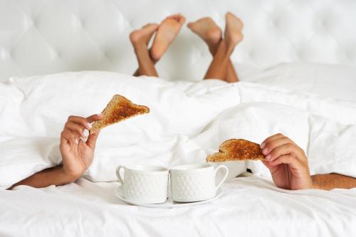a person laying in bed eating toast and cups of coffee at Base Napoli Mergellina in Naples