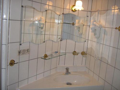 ein weiß gefliestes Bad mit einem Waschbecken und einem Spiegel in der Unterkunft Gasthaus Laubacher Wald in Laubach