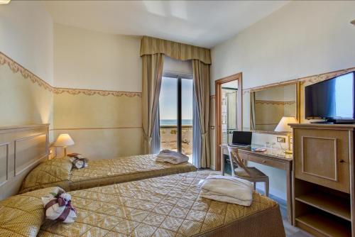 a hotel room with two beds and a desk and a television at Hotel Byron in Rimini