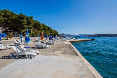 a row of chairs and umbrellas next to the water at Hotel Medena in Trogir