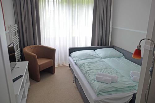 a small bedroom with a bed and a chair at G&H Hotel Rosengarten in Rosengarten