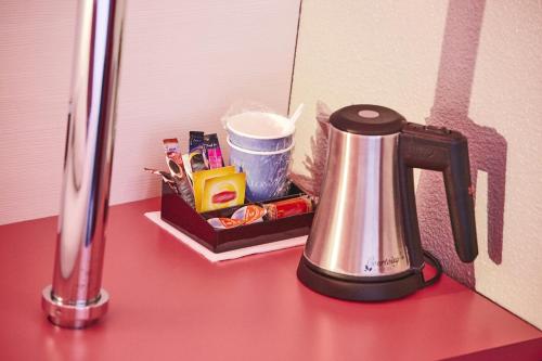a tea kettle sitting on a red counter with a container at Kyriad Hôtel La Fleche in La Flèche