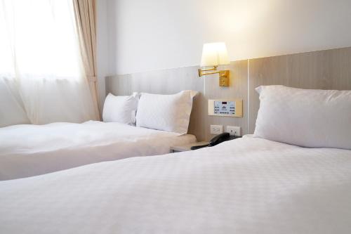 two beds in a hotel room with white sheets and pillows at Dynasty Hotel in Tainan