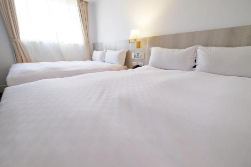 two beds in a hotel room with white sheets at Dynasty Hotel in Tainan