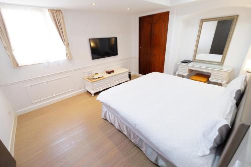 a bedroom with a white bed and a television at Dynasty Hotel in Tainan
