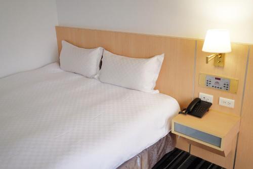 a bed in a hotel room with a phone on a table at Dynasty Hotel in Tainan