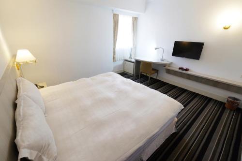 a hotel room with a large white bed and a desk at Dynasty Hotel in Tainan