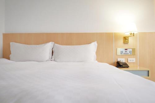 a large bed with white sheets and a telephone at Dynasty Hotel in Tainan