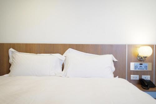 a white bed with white pillows and a lamp at Dynasty Hotel in Tainan