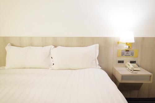 a bed with white pillows and a phone on a table at Dynasty Hotel in Tainan