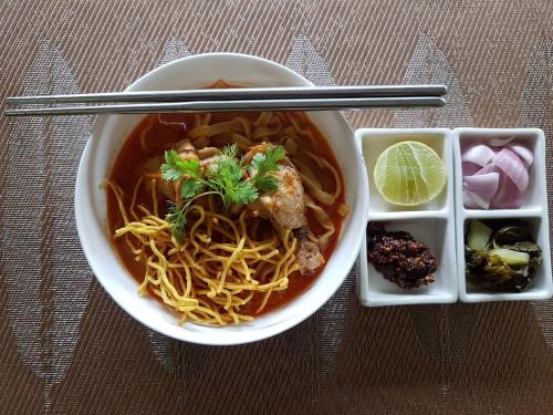 een kom soep met noedels en eetstokjes en een dienblad met eten bij Aruntara Riverside Boutique Hotel in Chiang Mai