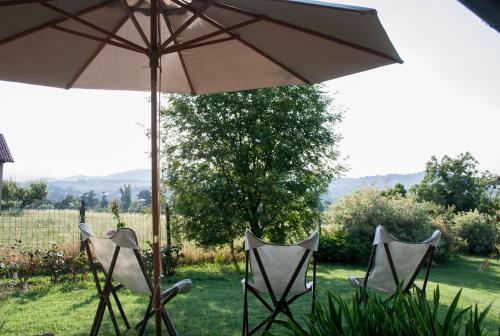 three chairs and an umbrella in the grass at B&B Puntodivista in Chieri