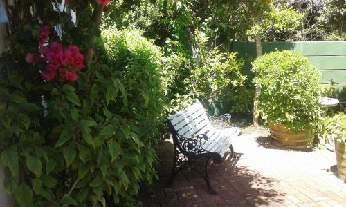 a white bench sitting in a garden with flowers at Eastbury Cottage in Hermanus