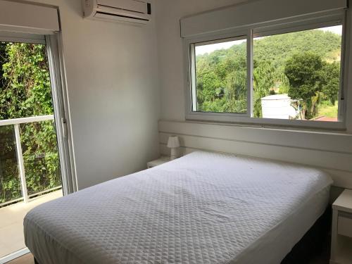 1 dormitorio blanco con 1 cama y 2 ventanas en Bombinhas Quinta do Mar Complexo B, en Bombinhas