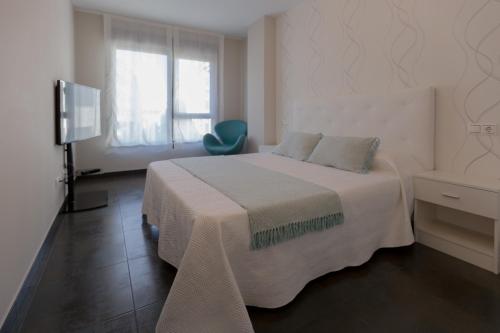 1 dormitorio blanco con 1 cama y 1 silla azul en Apartamento Playa Mar Portonovo Centro., en Sanxenxo
