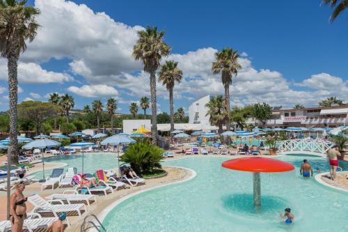 una piscina en un complejo con gente en sillas y palmeras en Riva Nuova Camping Village en Martinsicuro