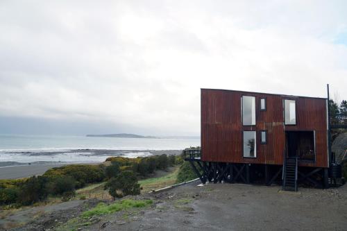 a house sitting on top of a hill next to the ocean at El Coo Lodge in Queilén