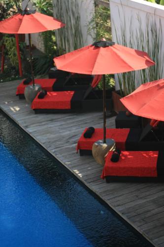 a row of red chairs with umbrellas next to a pool at Kamar Kamar Boutique Hotel in Seminyak