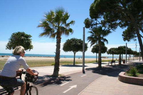 a woman riding a bike down a sidewalk near the beach at Camping Joan Bungalow Park in Cambrils