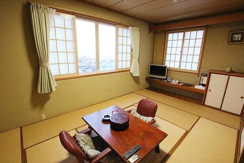 ein Wohnzimmer mit einem Tisch, Stühlen und Fenstern in der Unterkunft Hakodate Motomachi Hotel in Hakodate