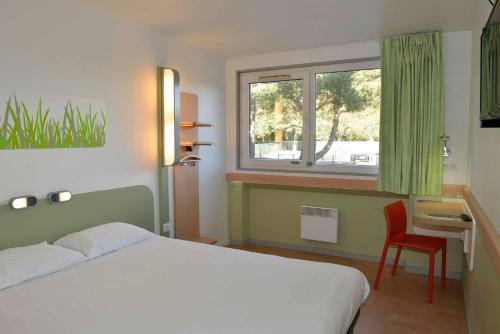 a bedroom with a bed and a window and a chair at ibis budget Bordeaux Lac in Bordeaux