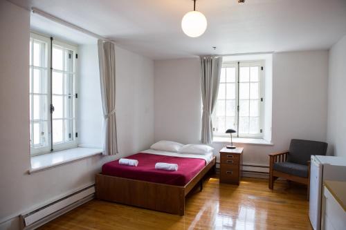 a bedroom with a bed and a chair and two windows at The Grey Nuns Residence by Concordia University in Montréal