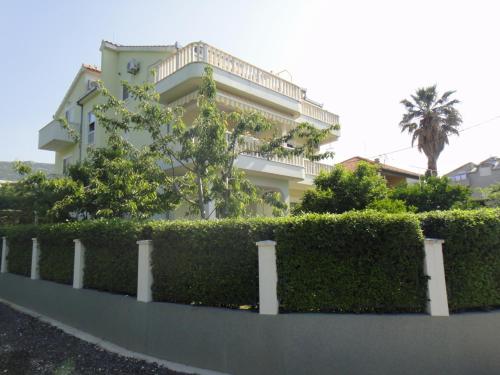 une maison blanche avec une haie devant elle dans l'établissement Apartments Roko, à Kaštela