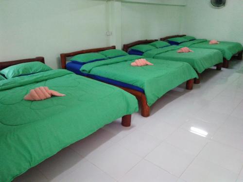 a row of four beds in a room with green covers at Baan Termsuk in Khao Kho