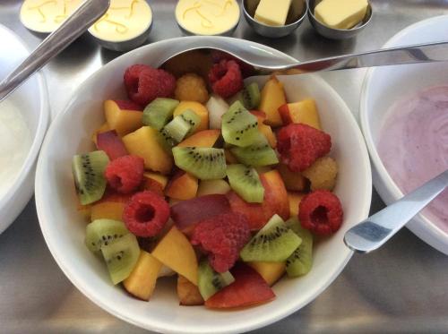 a bowl of fruit with raspberries and kiwis on a table at Tisza Lodge B&B - Panzió in Tiszaderzs