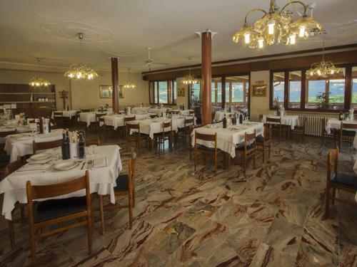 un restaurante con mesas y sillas blancas y lámparas de araña en Hotel Posta, en Rota d'Imagna