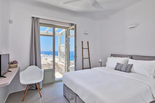 a white bedroom with a bed and a desk and a window at Tourlos Bay Villas Mykonos in Tourlos