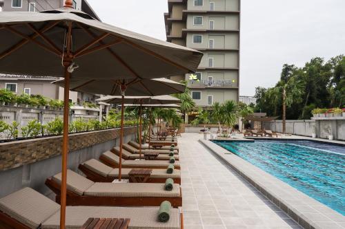 a pool with lounge chairs and umbrellas next to a building at Olive Tree Hotel Pattaya in Na Jomtien