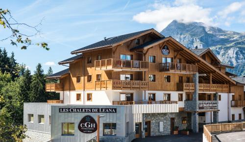 un grand bâtiment en bois avec des montagnes en arrière-plan dans l'établissement CGH Résidence Boutique Les Chalets de Léana, aux Carroz d'Arâches