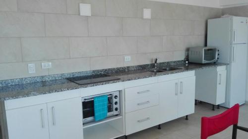 cocina con armarios blancos, fregadero y nevera en Costanera, en Santa Clara del Mar