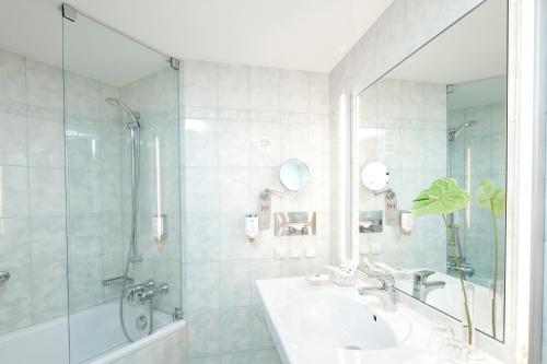 a white bathroom with a sink and a shower at Mercure Hotel Berlin Tempelhof in Berlin