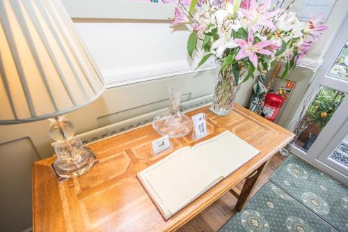 Park Lodge Guest House في وايتلي باي: طاولة عليها مصباح و إناء من الزهور