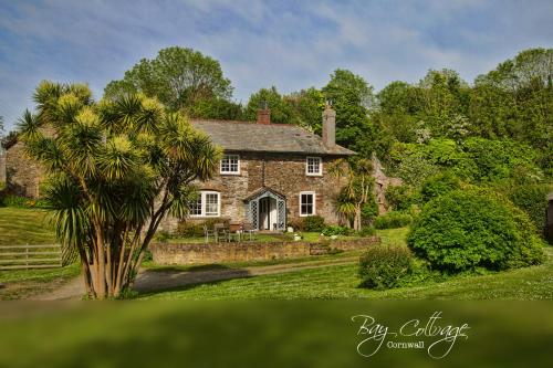 an old stone house with a palm tree in front of it at Bay Cottage & Bay Stables in Torpoint