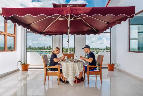 a man and woman sitting at a table under an umbrella at Rekidhiye Inn in Hithadhoo