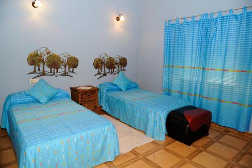 two beds in a room with blue sheets and blue curtains at El Rincón de Cabañeros in Retuerta de Bullaque