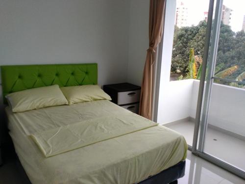 a bedroom with a bed with a green headboard and a window at Hotel Almond Beach in Tonsupa