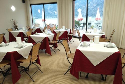 a dining room with tables with red and white tablecloths at Hotel Oasi Beach in Malcesine