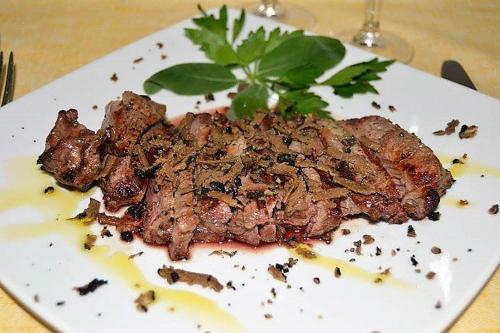 a piece of meat on a white plate on a table at Hotel Chenno in Subbiano
