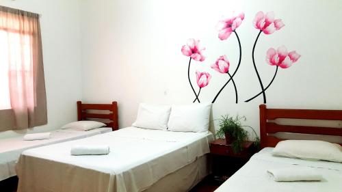 two beds in a room with pink flowers on the wall at Pousada Dom Aquino in Campo Grande