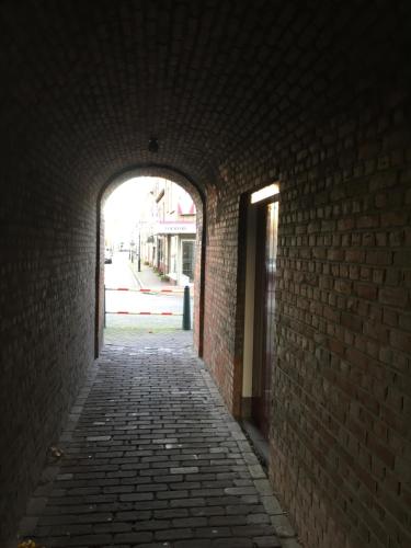 an alley with a brick wall and an arch way at De Stadspoort appartementen in Aardenburg