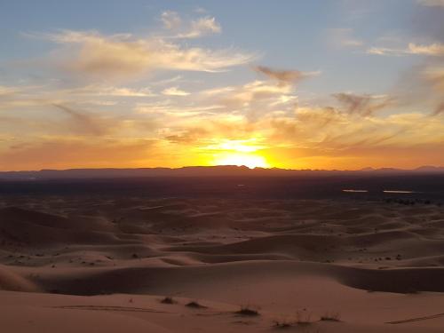 a sunset in the desert with the sun setting at Kasbah Erg Chebbi in Merzouga