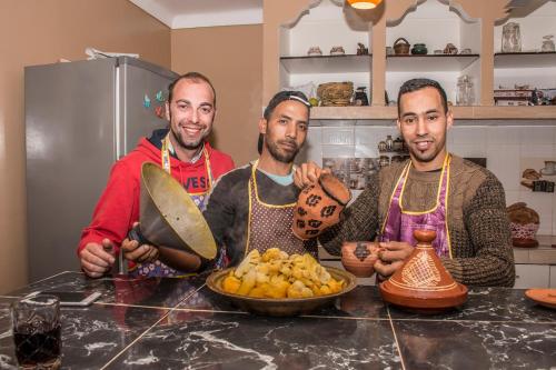 three men in a kitchen with a table with a bowl of food at Kasbah Red Castel Hostel in Marrakech