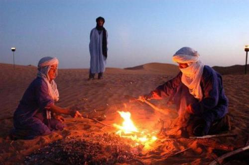 three people sitting around a fire in the desert at Camp Sahara Holidays in Mhamid