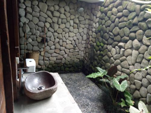 baño con pared de piedra y aseo en Melati Bali Homestay, en Canggu